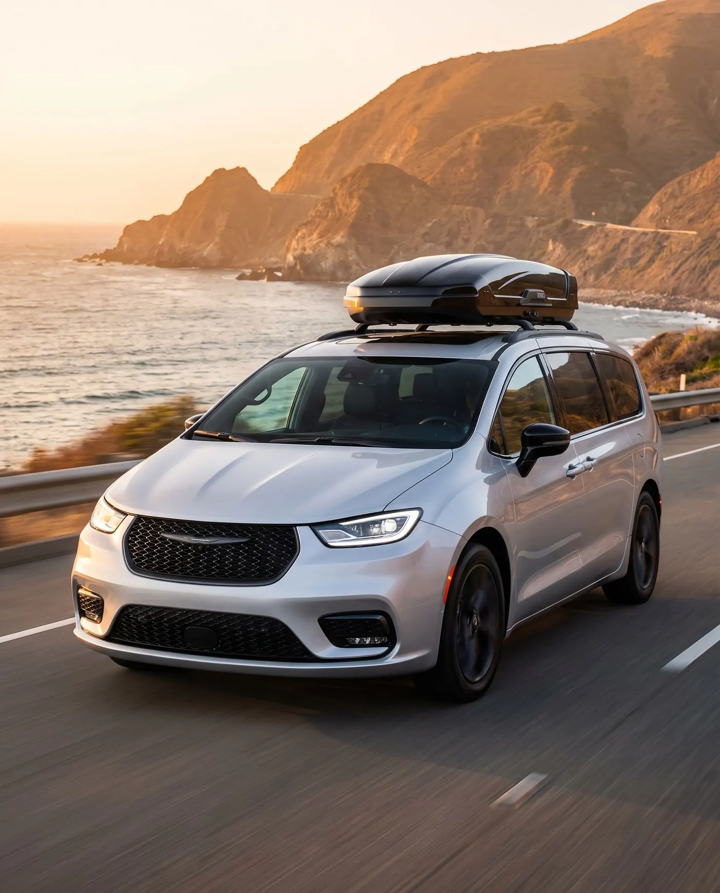 Chrysler Pacifica with a roof box on a coastal highway at golden hour